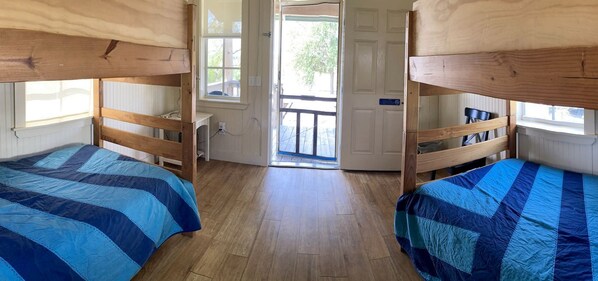 A room with bunk beds, wooden flooring, and a door leading outside.