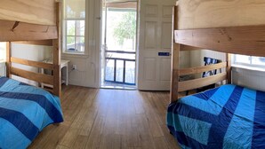 A room with bunk beds, wooden flooring, and a door leading outside.