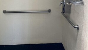 A bathroom with a grab bar, a shower control panel, and a metal shelf.