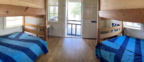 A room with bunk beds, wooden flooring, and a door leading outside.