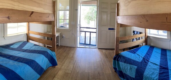 A room with bunk beds, wooden flooring, and a door leading outside.