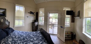 A bedroom with a bed, a desk, a chair, a television, and a door leading to an outdoor deck. - Lakefront Cabin Rental in Bradenton, Florida (Bradenton)