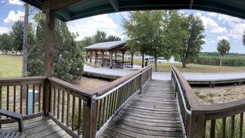 Una terraza de madera con vista a un parque, que incluye un pabellón y mesas de picnic.