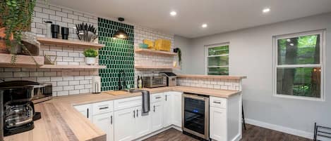 A modern kitchen with white cabinets, a green backsplash, wooden countertops, and a built-in oven.
