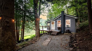 Une cabane dotée d’un porche, entourée d’arbres et bordée d’un chemin de gravier.