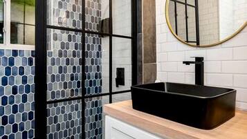Een moderne badkamer met een zwart wastafelmeubel, witte kasten en een douchecabine van glas.