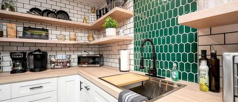 A kitchen with white cabinets, a wooden countertop, a green hexagonal backsplash, and a stainless steel sink.