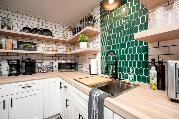 A kitchen with white cabinets, a wooden countertop, a green hexagonal backsplash, and a stainless steel sink.