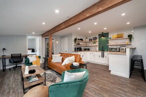A modern living room with a sofa, chairs, a coffee table, and a kitchen in the background.
