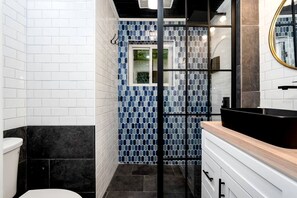 A bathroom with white tiled walls, a black bathtub, a wooden vanity, and a blue-tiled shower area. - Scenic Retreat: Riverfront Cabin with Large Deck and Fire Pit in Emlenton, Pennsylvania (Emlenton)