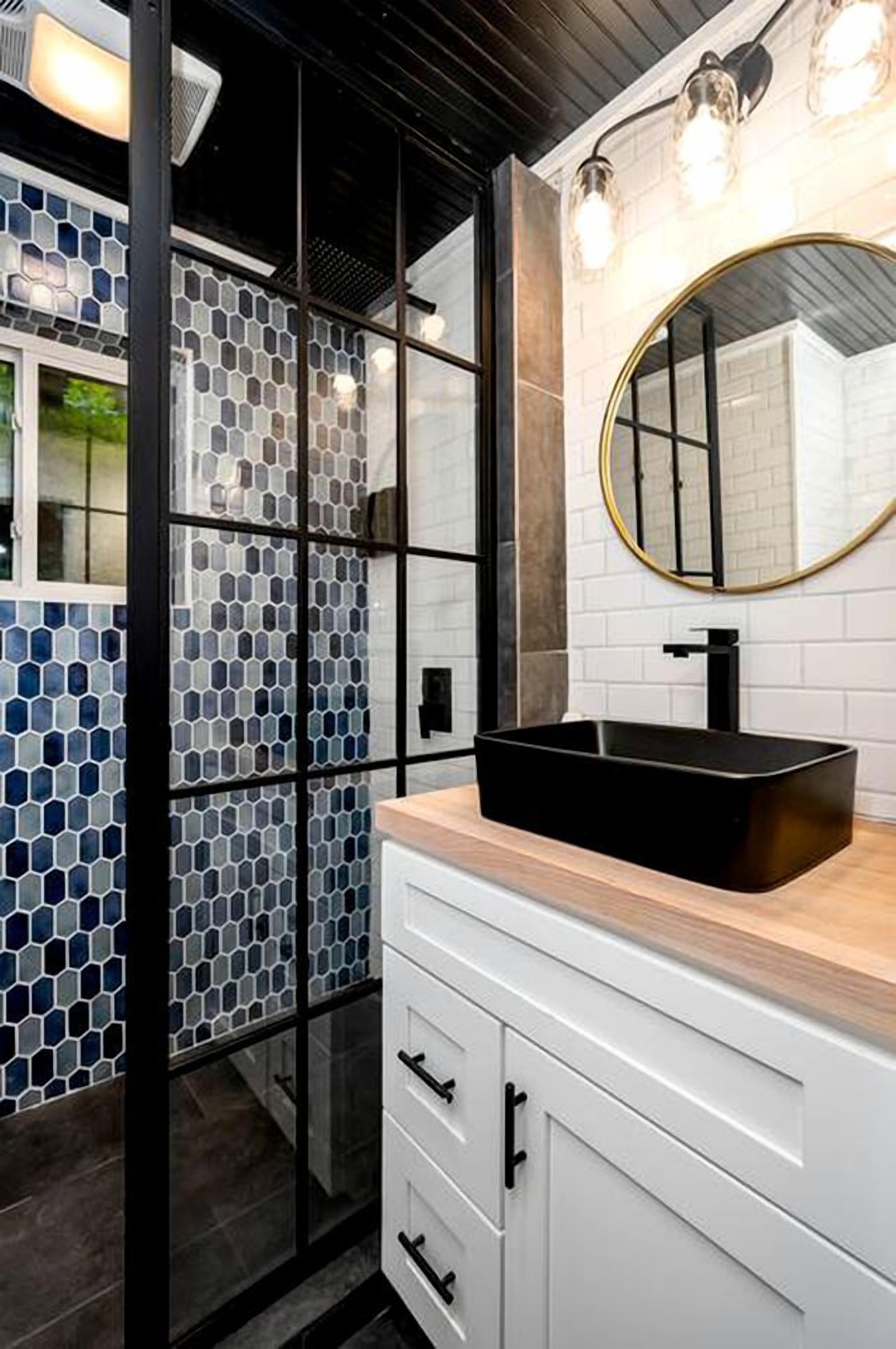 Un baño moderno con un lavabo negro, armarios blancos y una mampara de cristal.