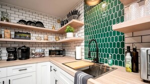 Cucina con mobili bianchi, un piano di lavoro in legno, una schiena di superficie esagonale verde e un lavello in acciaio inossidabile.