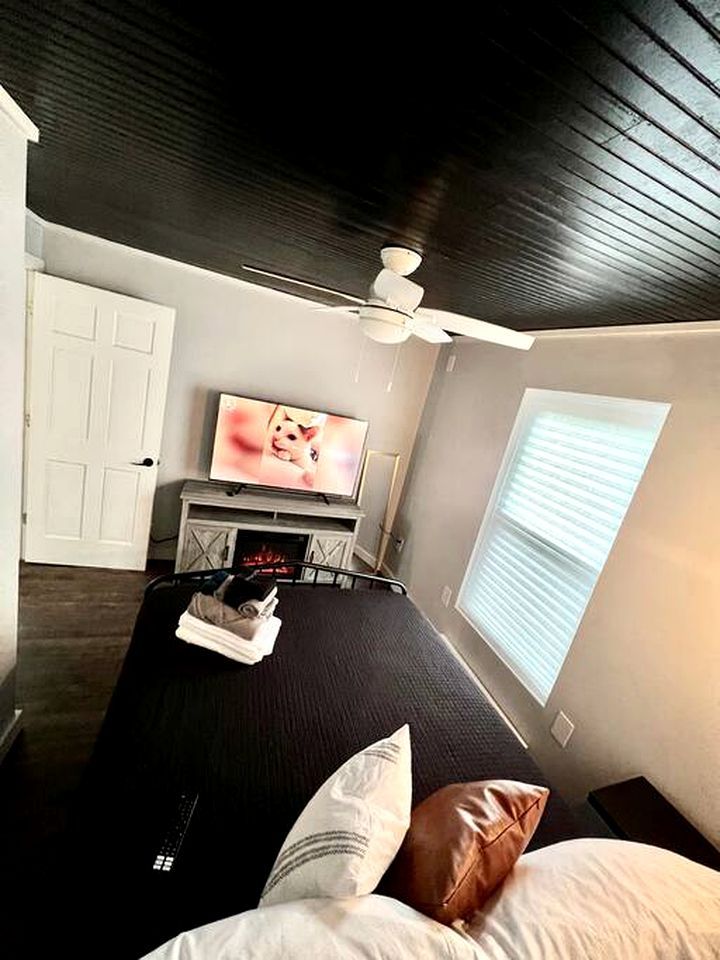 A bedroom with a bed, a TV, a ceiling fan, a window, and a door.