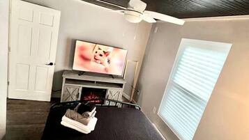 A bedroom with a bed, a TV, a ceiling fan, a window, and a door.