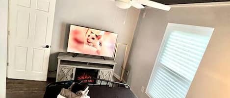 A bedroom with a bed, a TV, a ceiling fan, a window, and a door.