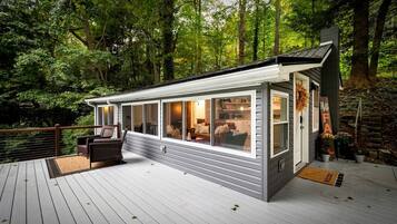 Eine moderne Holzhütte mit großen Fenstern, einer Terrasse und einem freundlichen Willkommensschild.