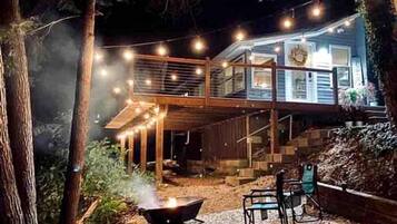 A two-story house with a deck, surrounded by trees, and string lights.