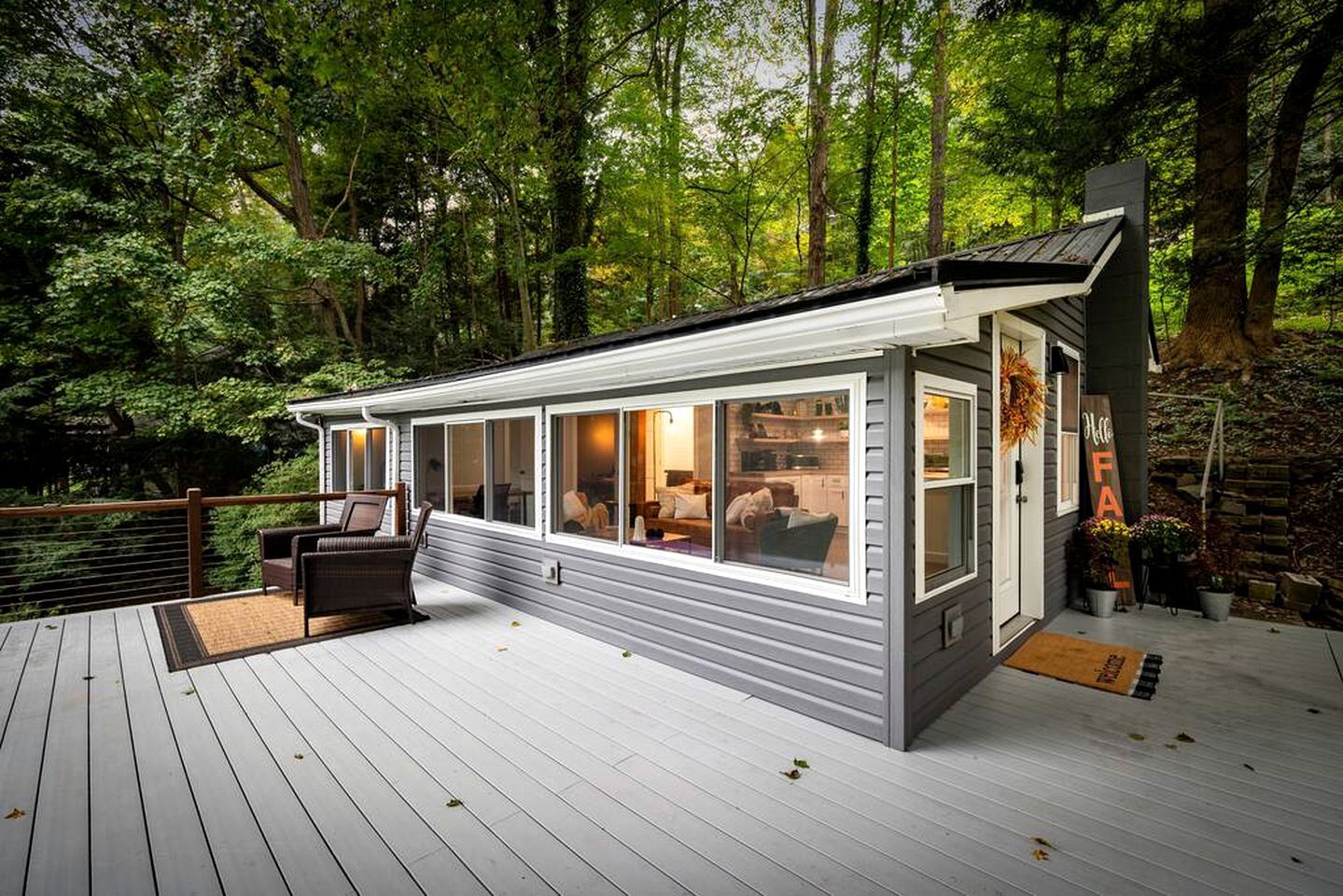 A modern cabin with large windows, a deck, and a welcoming sign.