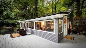 A modern cabin with large windows, a deck, and a welcoming sign.