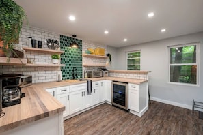 Una cocina moderna con armarios blancos, salpicadero verde, encimeras de madera y horno empotrado.