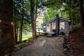 A cabin with a porch, surrounded by trees and a gravel path.