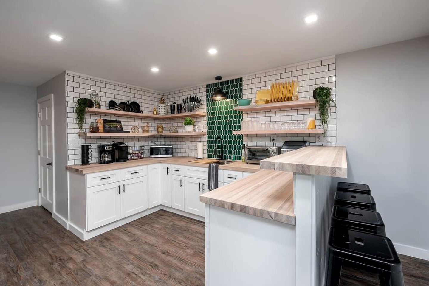A modern kitchen with white cabinets, wooden countertops, and a green backsplash.