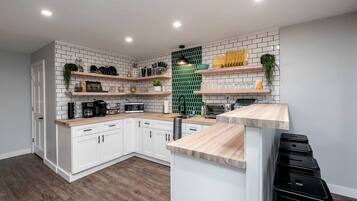 A modern kitchen with white cabinets, wooden countertops, and a green backsplash.