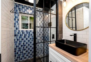 A bathroom with a tiled wall, a window, a sink, and a mirror.