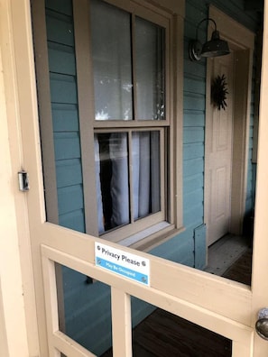 Una puerta con letrero de privacidad, una ventana y una lámpara fijada a la pared.