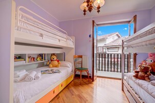 Camera a letto a castello per bambini, con pavimento in legno, una sedia, un orsacchiotto e una libreria.