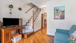 A living room with a wooden TV stand, a blue sofa, a staircase, and a wall-mounted picture. - Maison Rosamunda for 6 With Garden (Oulx)