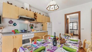 A kitchen with wooden cabinets, a stove, and a dining table set with plates and a bottle. - Maison Rosamunda for 6 With Garden (Oulx)