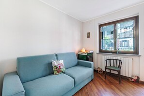 A room with a blue sofa, a wooden chair, a radiator, and a window with a view of buildings. - Maison Rosamunda for 6 With Garden (Oulx)