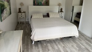 A bedroom with a large bed, two bedside tables, a nightstand, a painting on the wall, and a mirror.