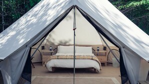 A tent with a bed, bedside tables, and a window.