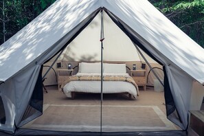 A tent with a bed, bedside tables, and a window.