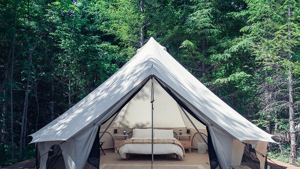 A tent with a bed, wooden deck, and forest background.