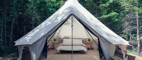 A tent with a bed, wooden deck, and forest background.