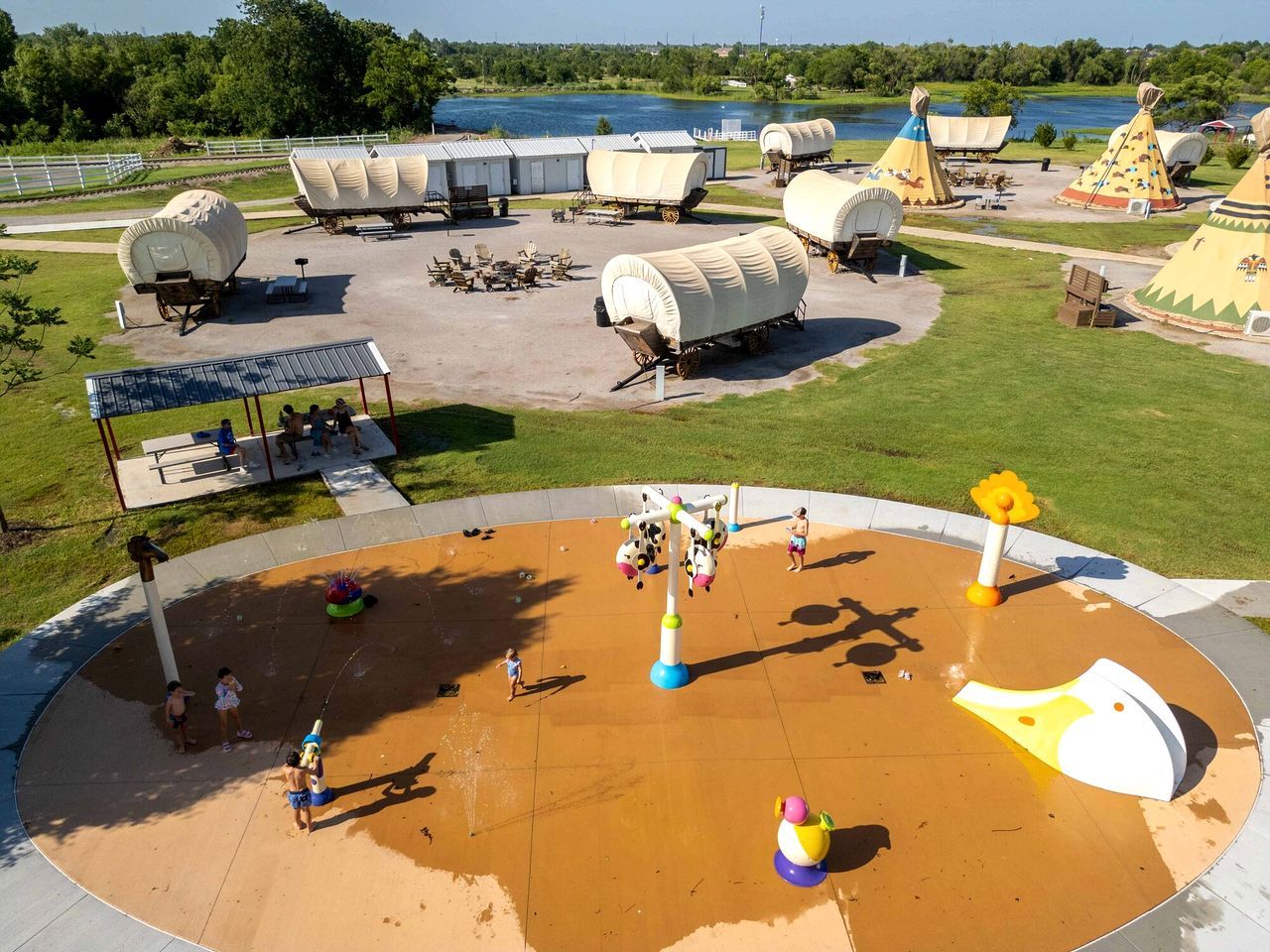A water park with a circular play area, picnic tables, and covered wagons in the background.