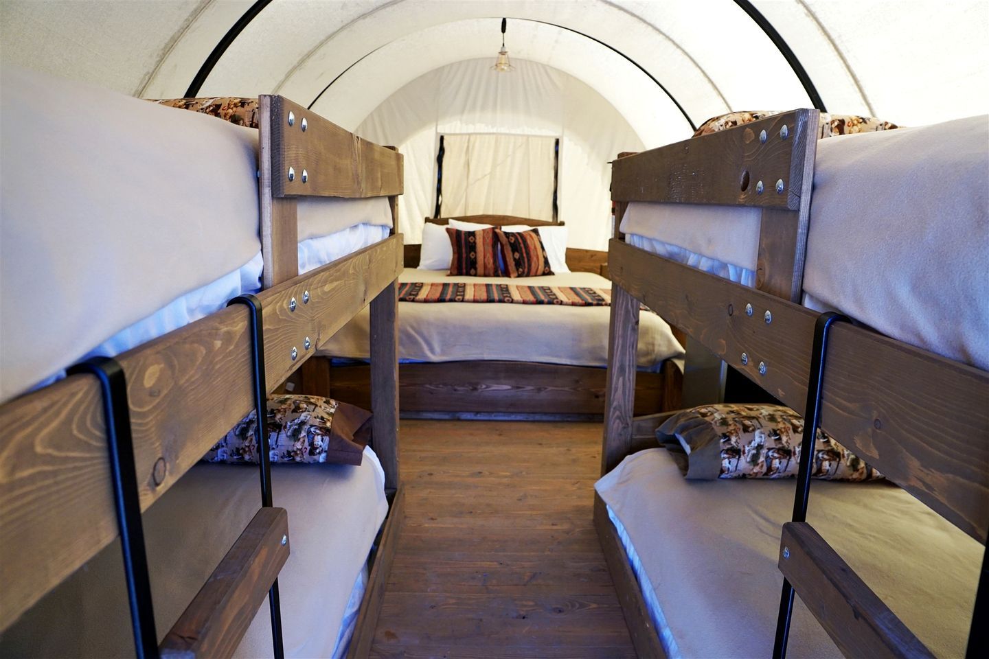 Ein Zelt mit Etagenbetten, Holzwandungen und einem zentralen Bett mit Kissen und Decke.