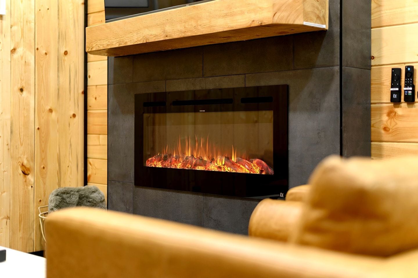 Une cheminée moderne avec une façade en verre, un lambris en bois sur les murs et une télécommande située à droite.