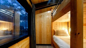 A cabin interior with a wooden floor, a bed with white bedding, a window with a view of trees, and a curtain. - Garage Loft • King + Bunks • Budget Friendly near Beavers Bend National Park (Broken Bow)