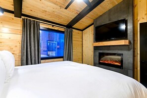 Un dormitorio con cama, chimenea, televisor y ventana con cortinas.