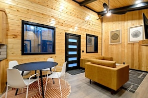 A wooden interior with a round table, white chairs, a sofa, and framed artwork on the walls. - Garage Loft • King + Bunks • Budget Friendly near Beavers Bend National Park (Broken Bow)