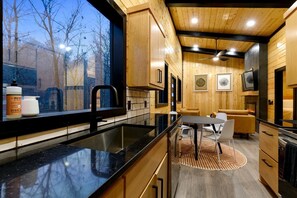 A modern kitchen with a black countertop, wooden cabinets, and a dining area with a round rug.