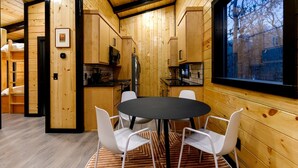 A wooden interior with a round table and chairs, a kitchen area, and a window with a view. - Garage Loft • King + Bunks • Budget Friendly near Beavers Bend National Park (Broken Bow)