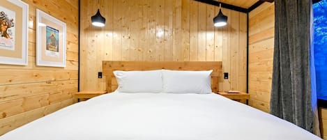 Una habitación con paneles de madera, una cama, dos lámparas colgantes y cuadros en la pared.