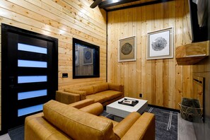 A wooden interior with a sofa, a coffee table, and framed artwork on the wall. - Garage Loft • King + Bunks • Budget Friendly near Beavers Bend National Park (Broken Bow)