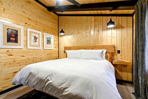 A wooden-paneled room with a bed, framed pictures on the wall, and a nightstand.