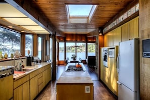 A modern kitchen with wooden cabinets, a central island, a refrigerator, and a view of a lake.